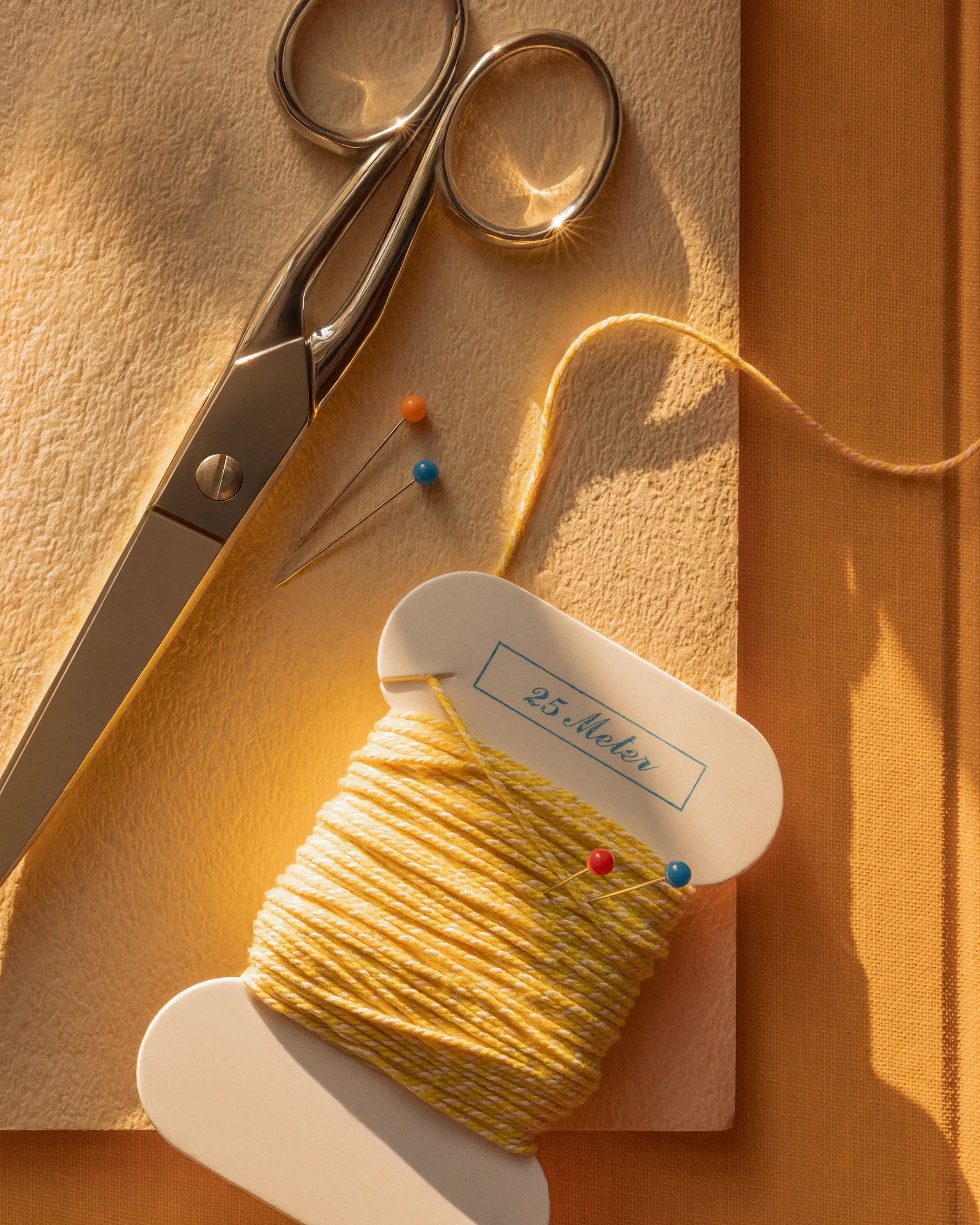 Sewing tools with yellow thread spool and pins in warm sunlight