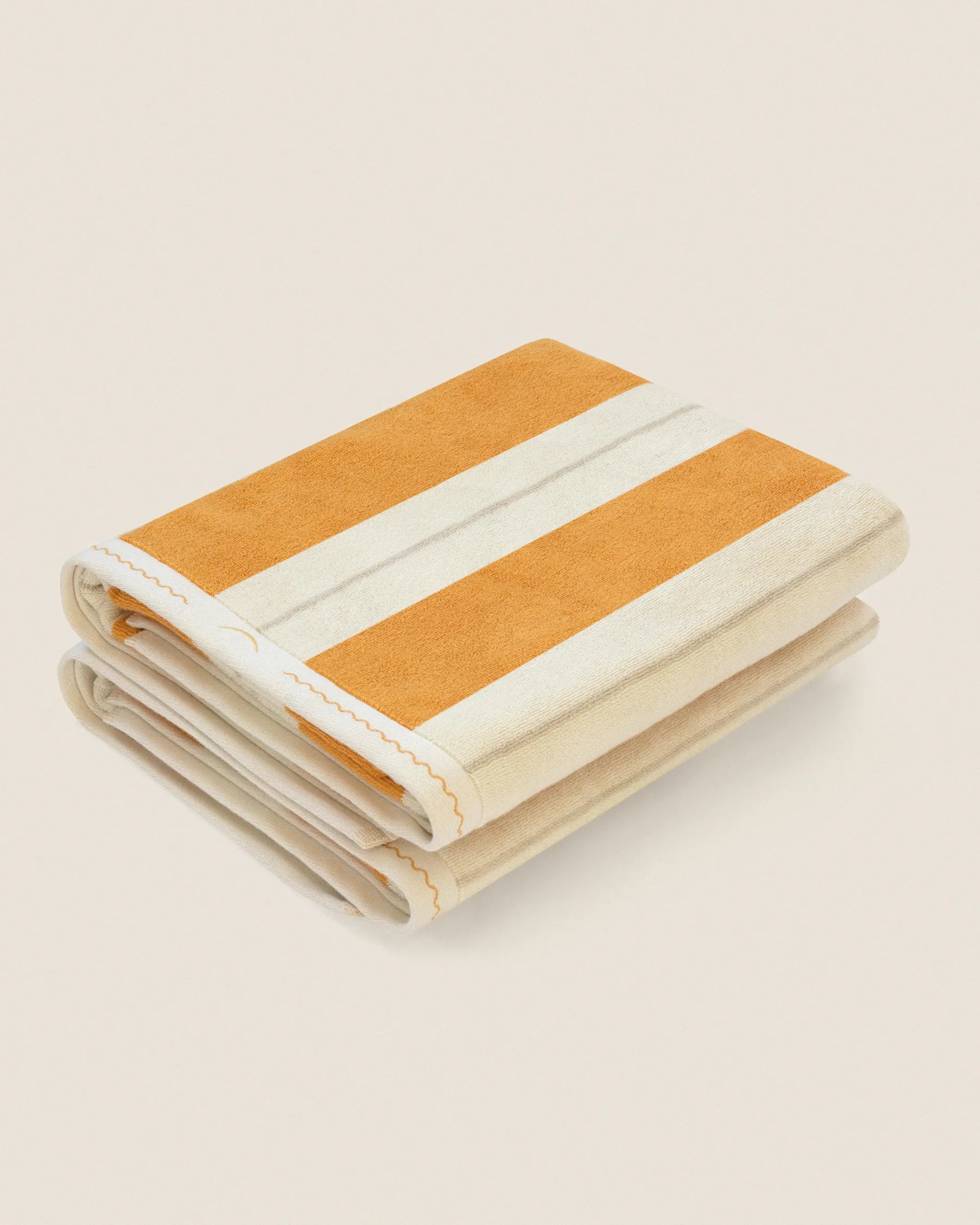 Folded pair of Éteanne Anné striped beach towel in Tuscan Sun on neutral background