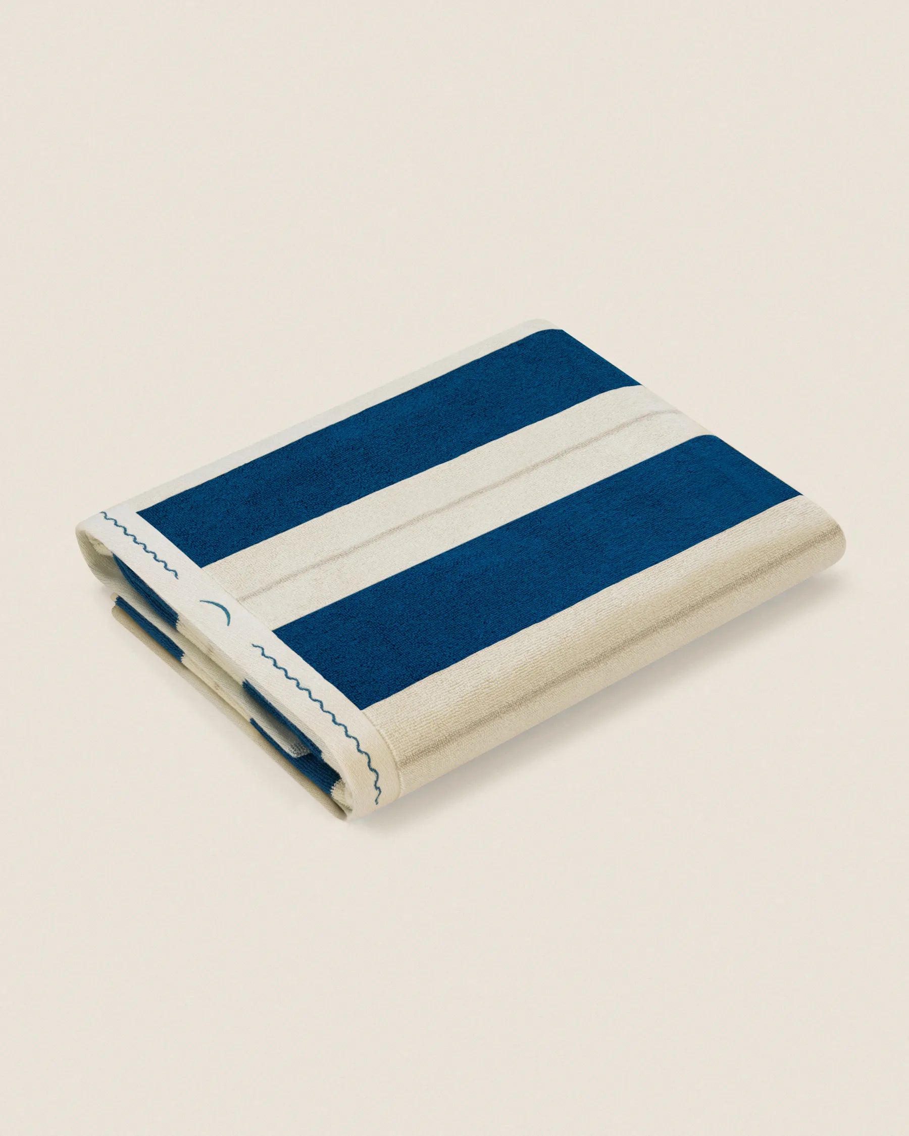 Folded Éteanne Anné striped beach towel in Ora Blu on neutral background