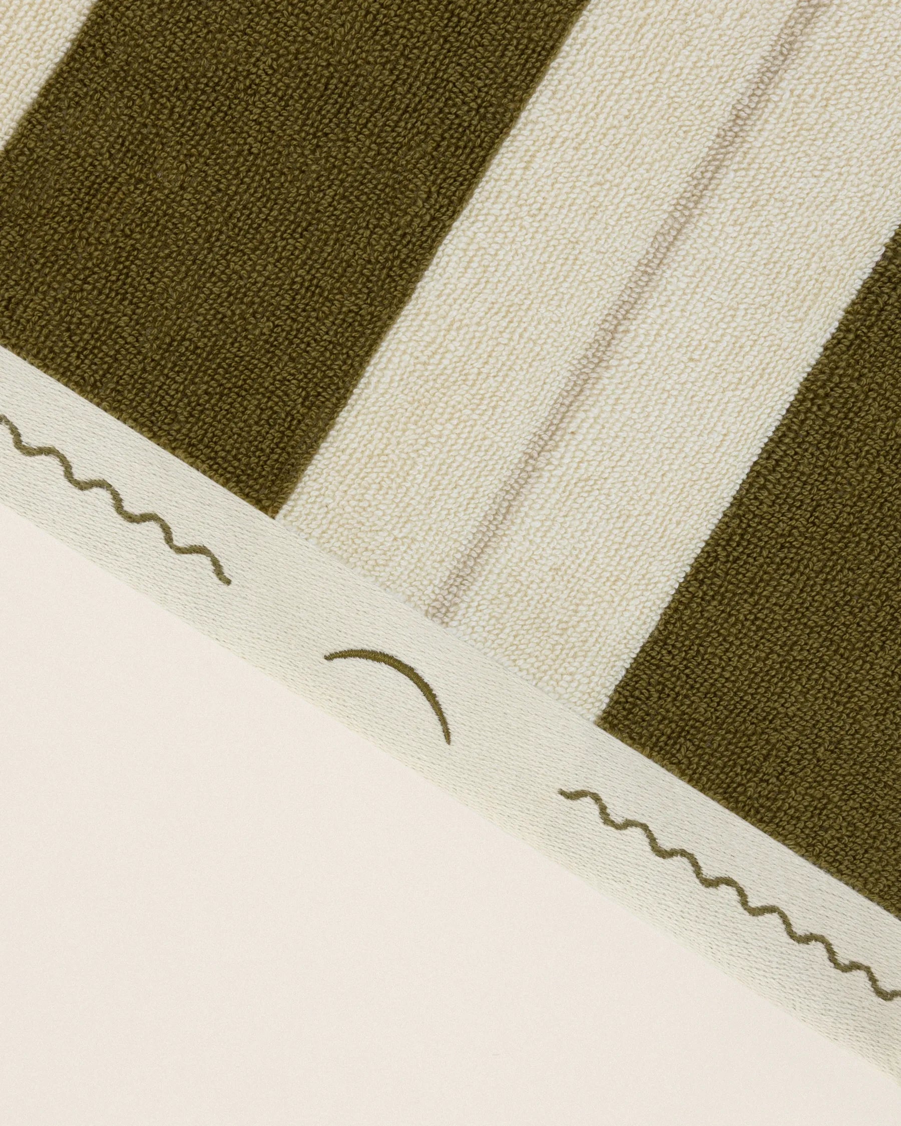 Close-up of striped beach towel edge with embroidered monogram in Terre Verte and Ionian Pearl
