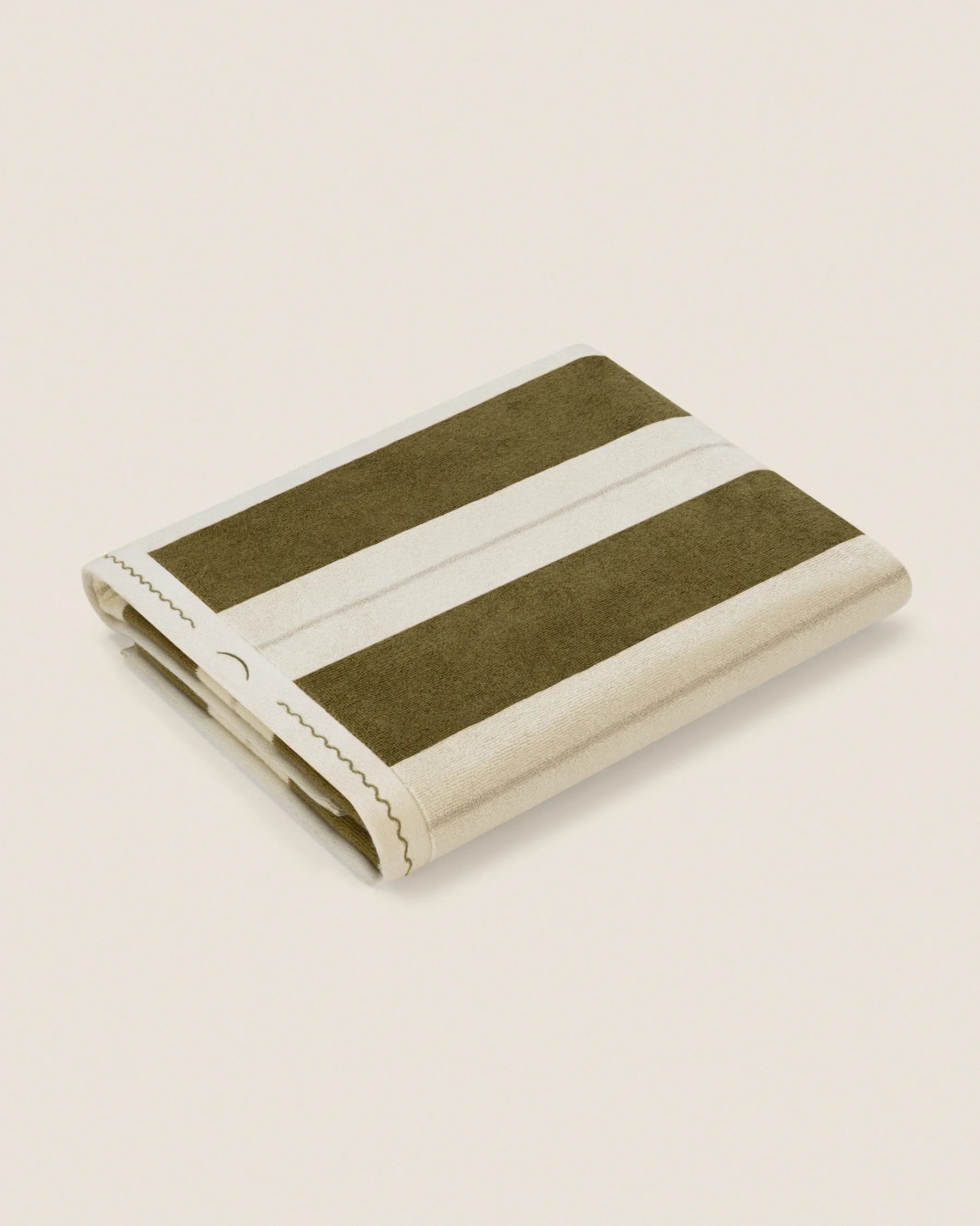 Folded Éteanne Anné striped beach towel in Terre Verte on neutral background