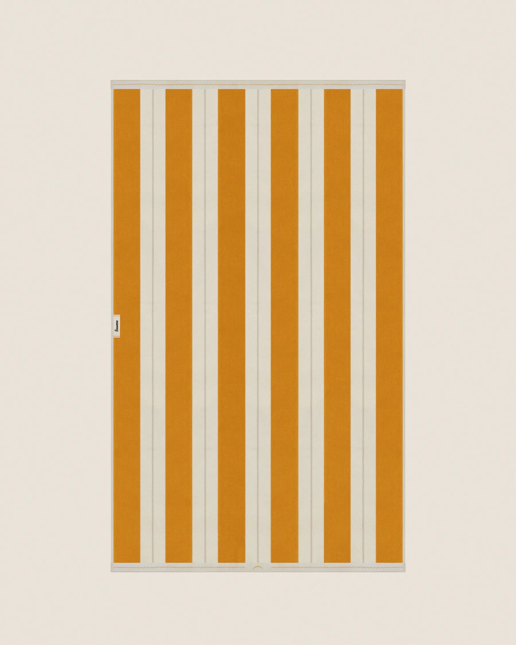 Striped beach towel in Tuscan Sun and Ioanian Pearl, laid flat on a neutral background