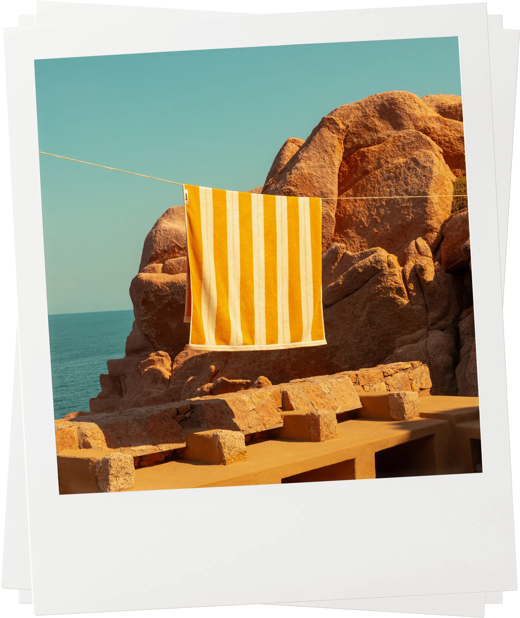 Éteanne striped beach towels in Tuscan Sun hanging outdoors by rocky coastline