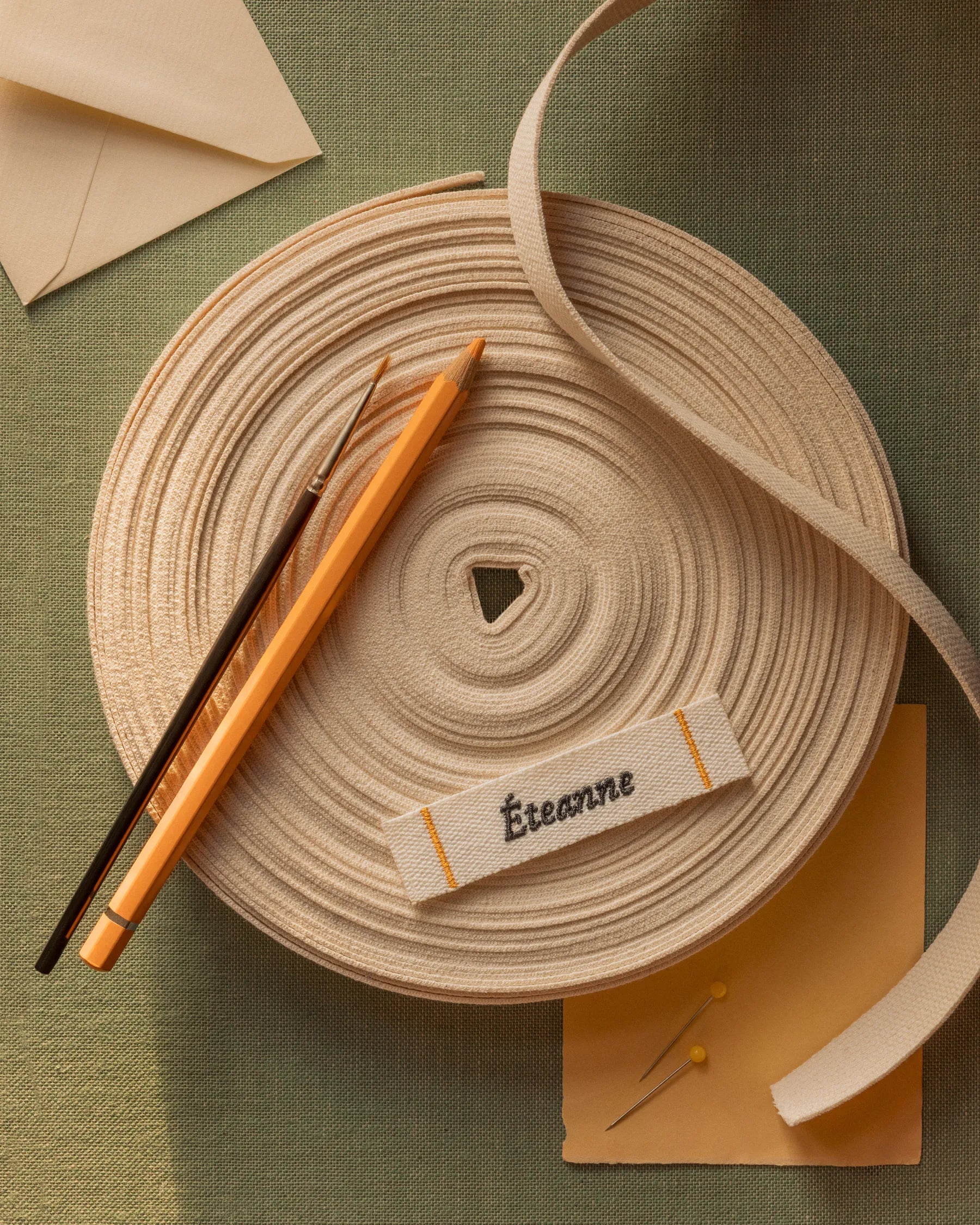 Éteanne woven label with cotton tape roll and sewing tools on textured fabric