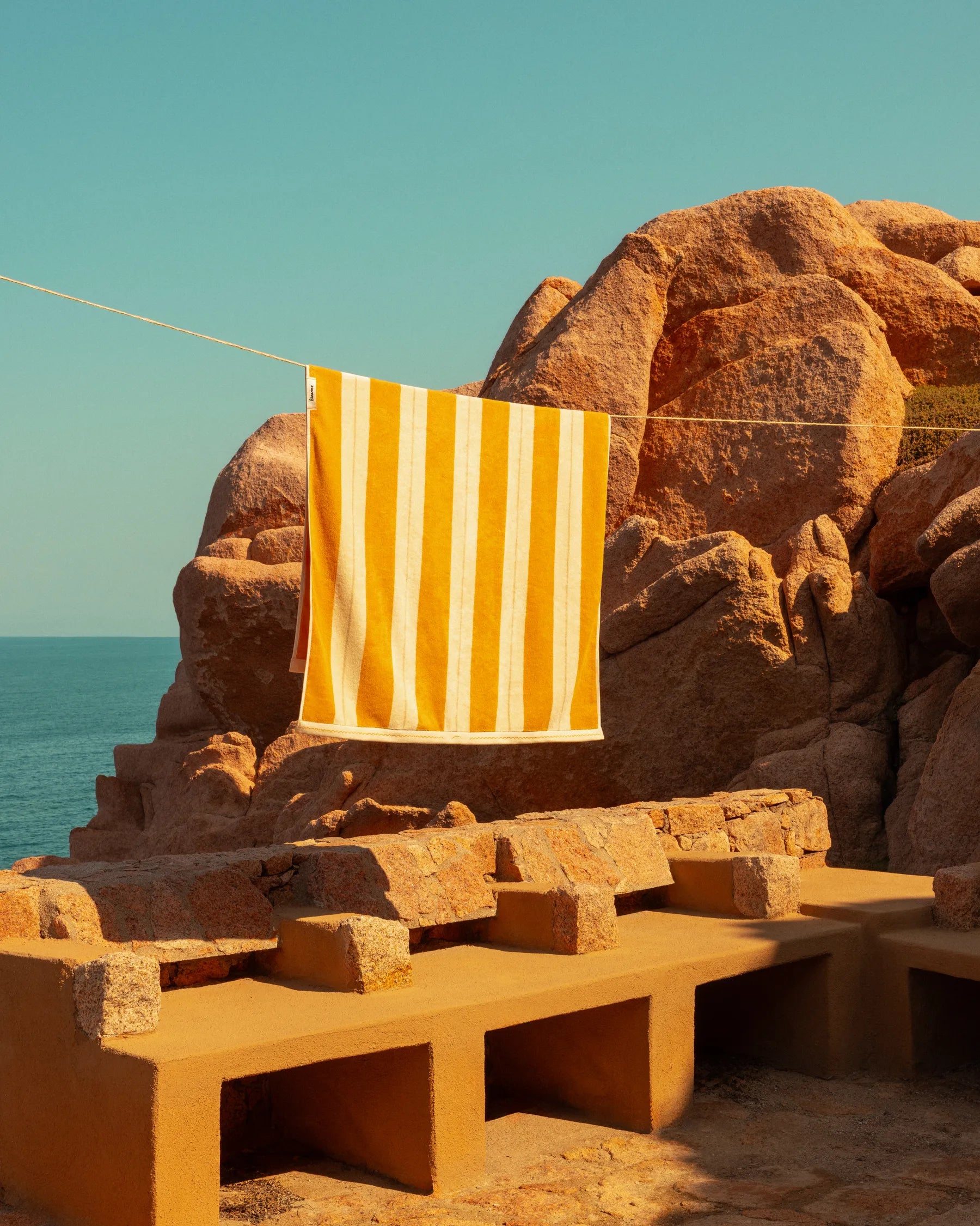 Éteanne striped beach towels in Tuscan Sun hanging outdoors by rocky coastline