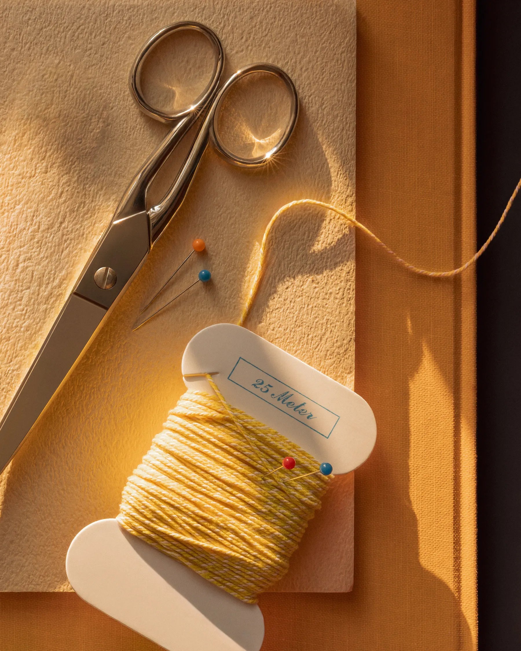 Sewing scissors, pins, and yellow thread in warm sunlight