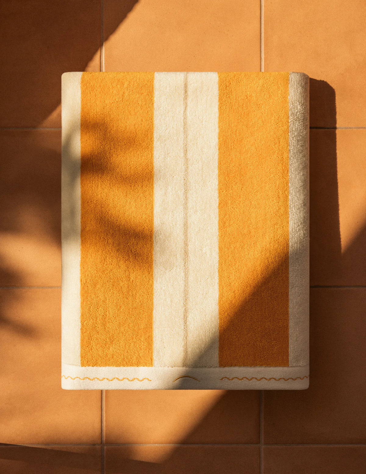 Folded Éteanne Anné striped beach towel in Tuscan Sun on terracotta floor.