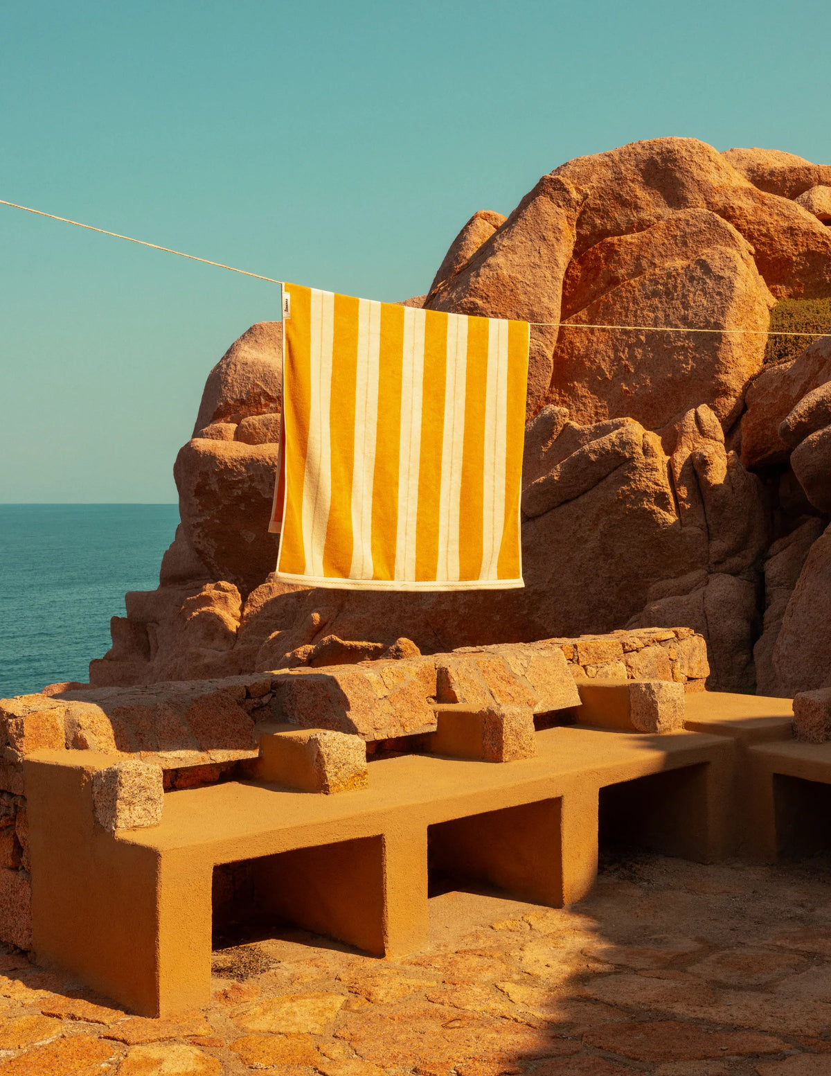Éteanne striped beach towels in Tuscan Sun hanging outdoors by rocky coastline