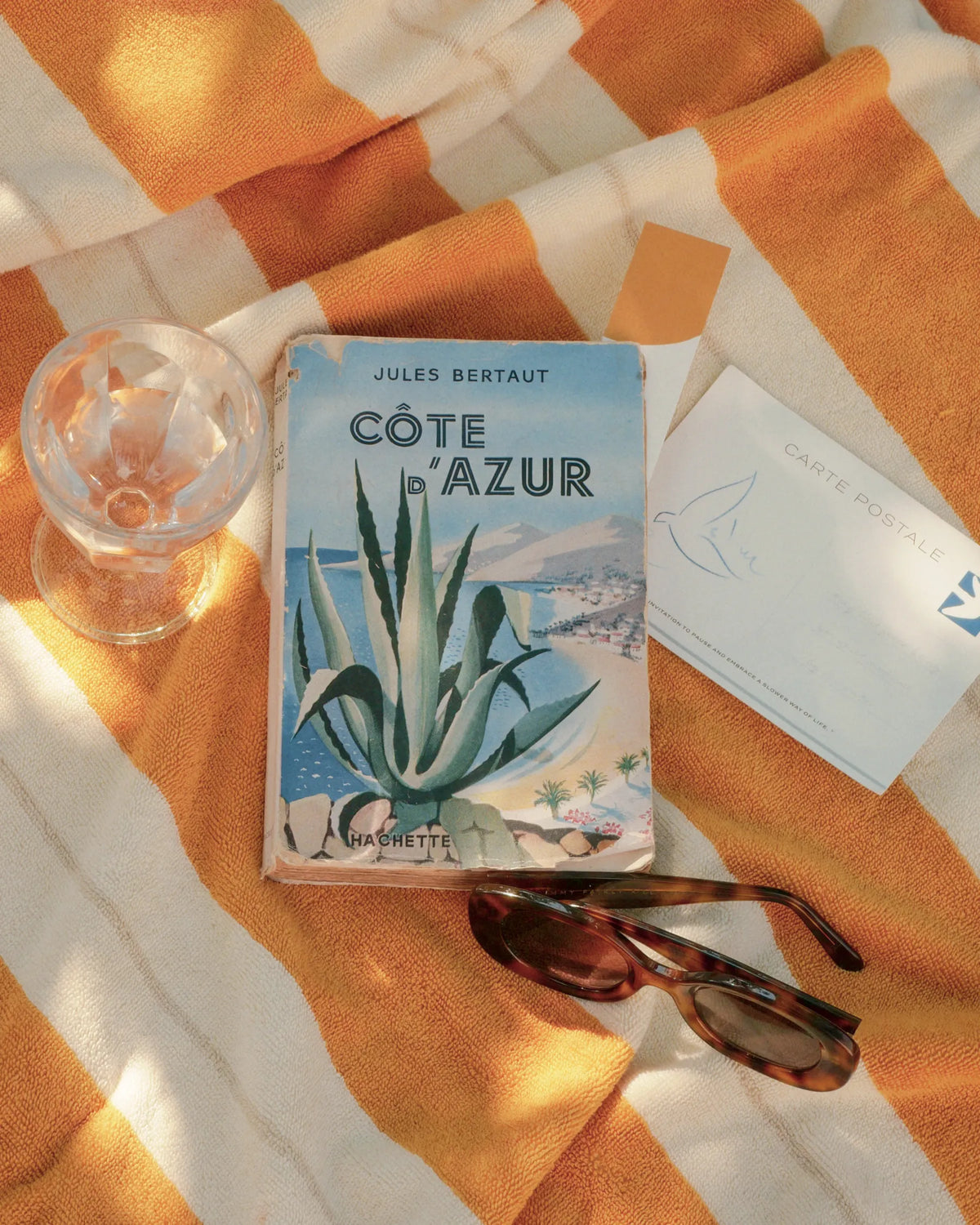 Vintage Côte d’Azur book, sunglasses and postcard on Éteanne striped beach towel in Tuscan Sun