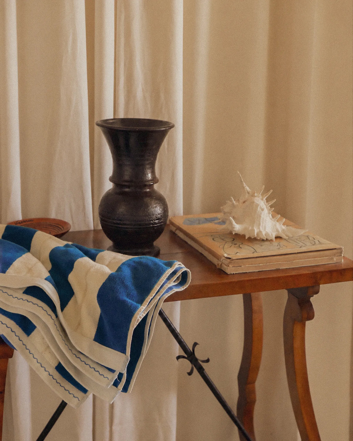 Éteanne striped beach towel in Ora Blu draped over a vintage table