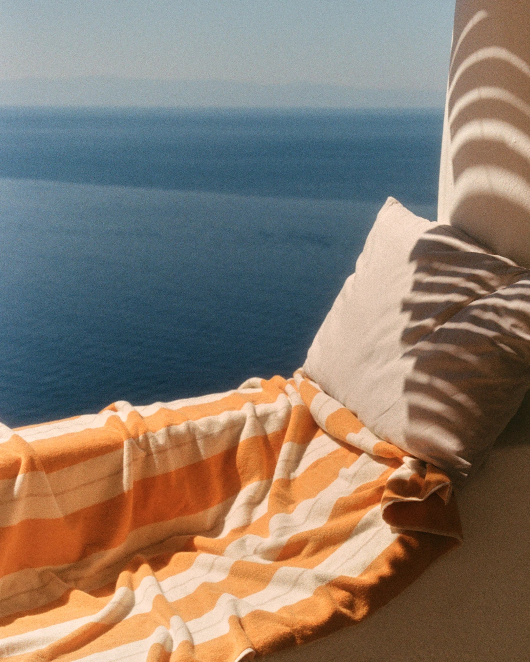 Anne Beach Towel in Tuscan Sun draped across a white Mediterranean terrace overlooking the sea.