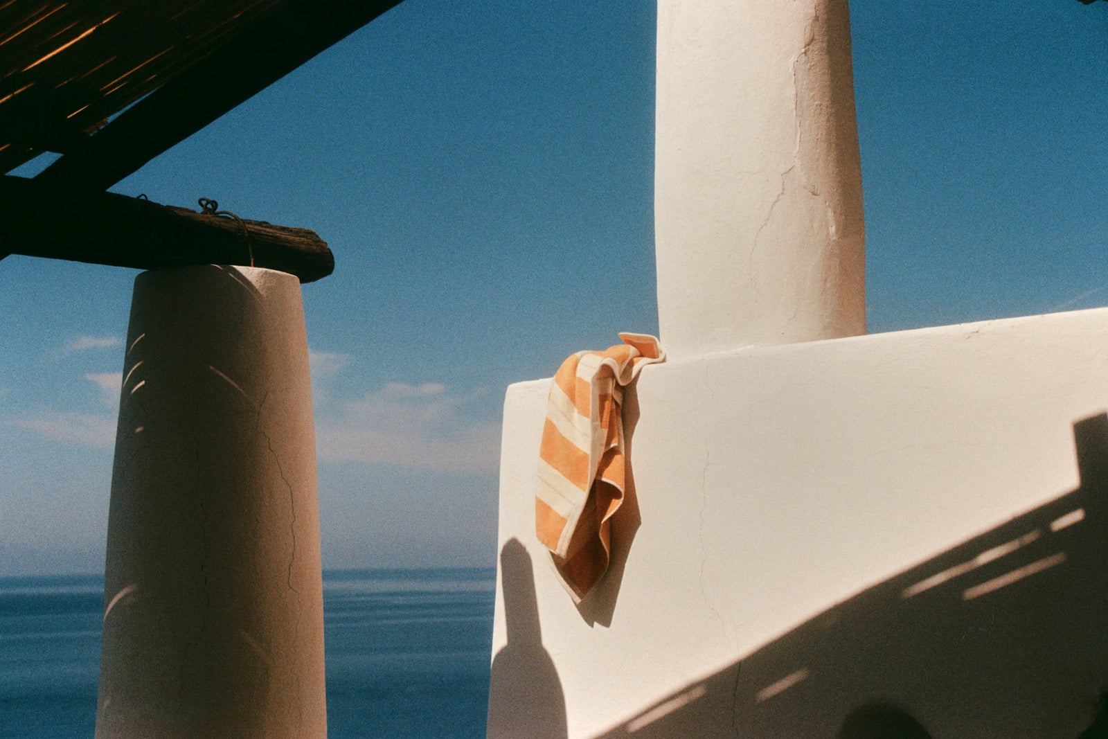 Anne Beach Towel in Tuscan Sun draped over a white Mediterranean terrace overlooking the sea.