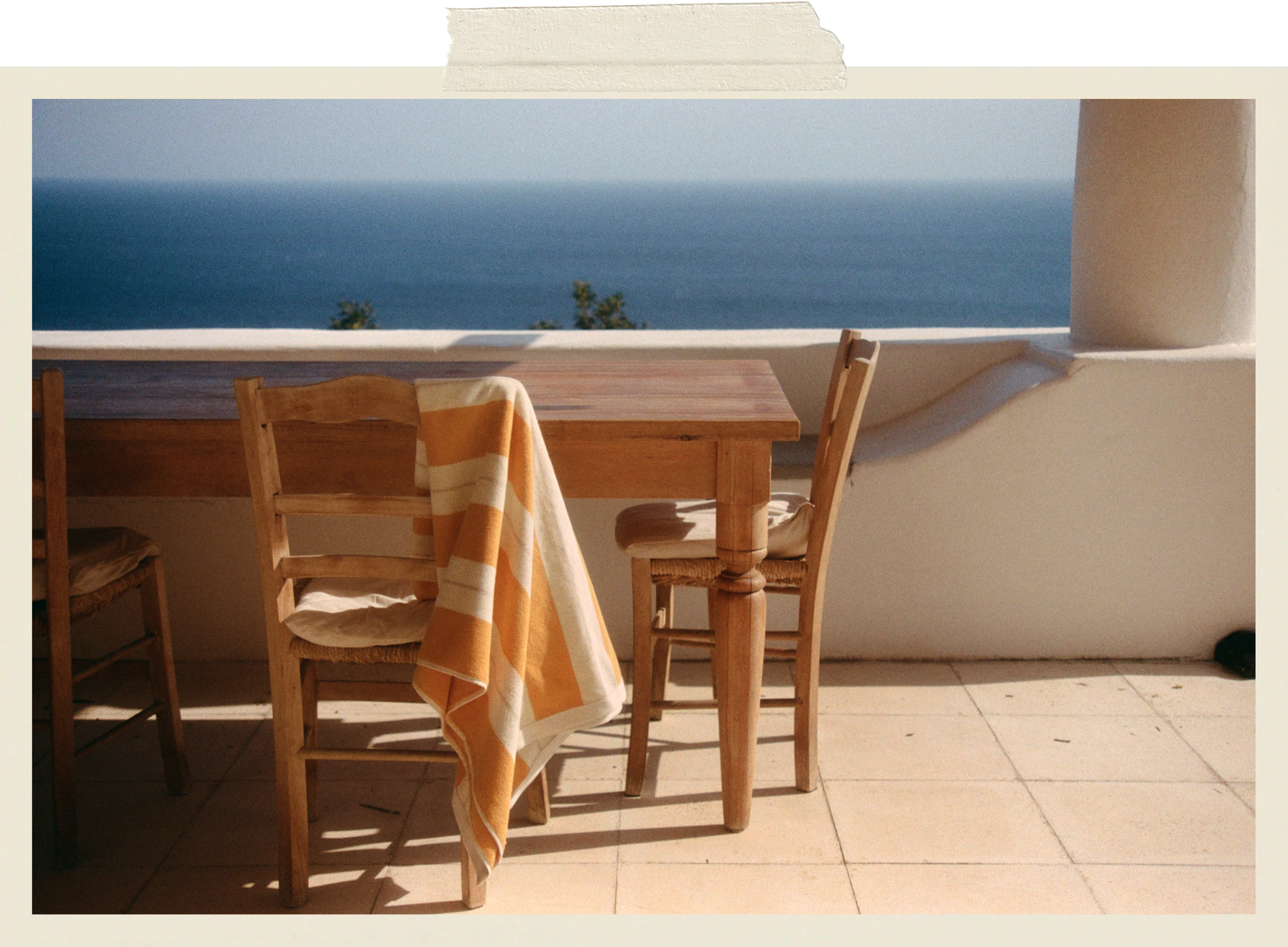 Anne Beach Towel in Tuscan Sun draped over a wooden chair on a Mediterranean terrace overlooking the sea.