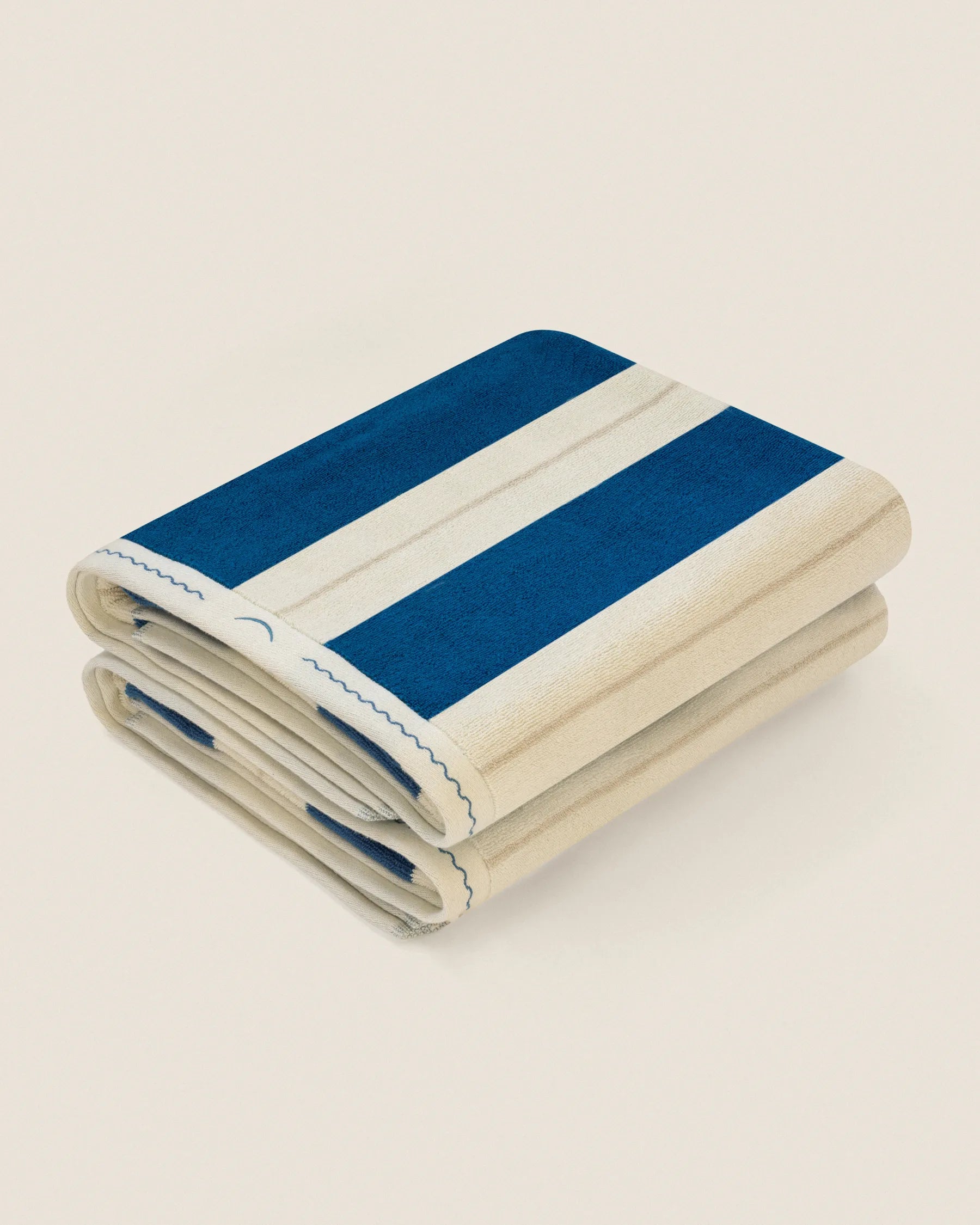 Folded pair of Éteanne Anné striped beach towel in Ora Blu on neutral background