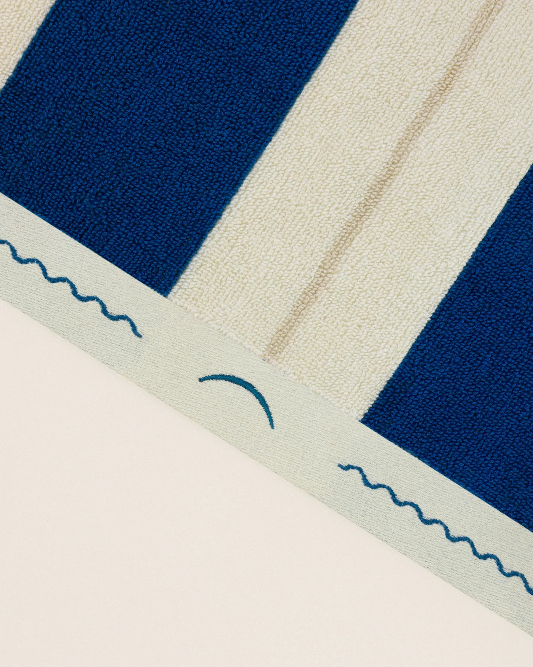 Close-up of striped beach towel edge with embroidered monogram in Ora Blu and Ionian Pearl