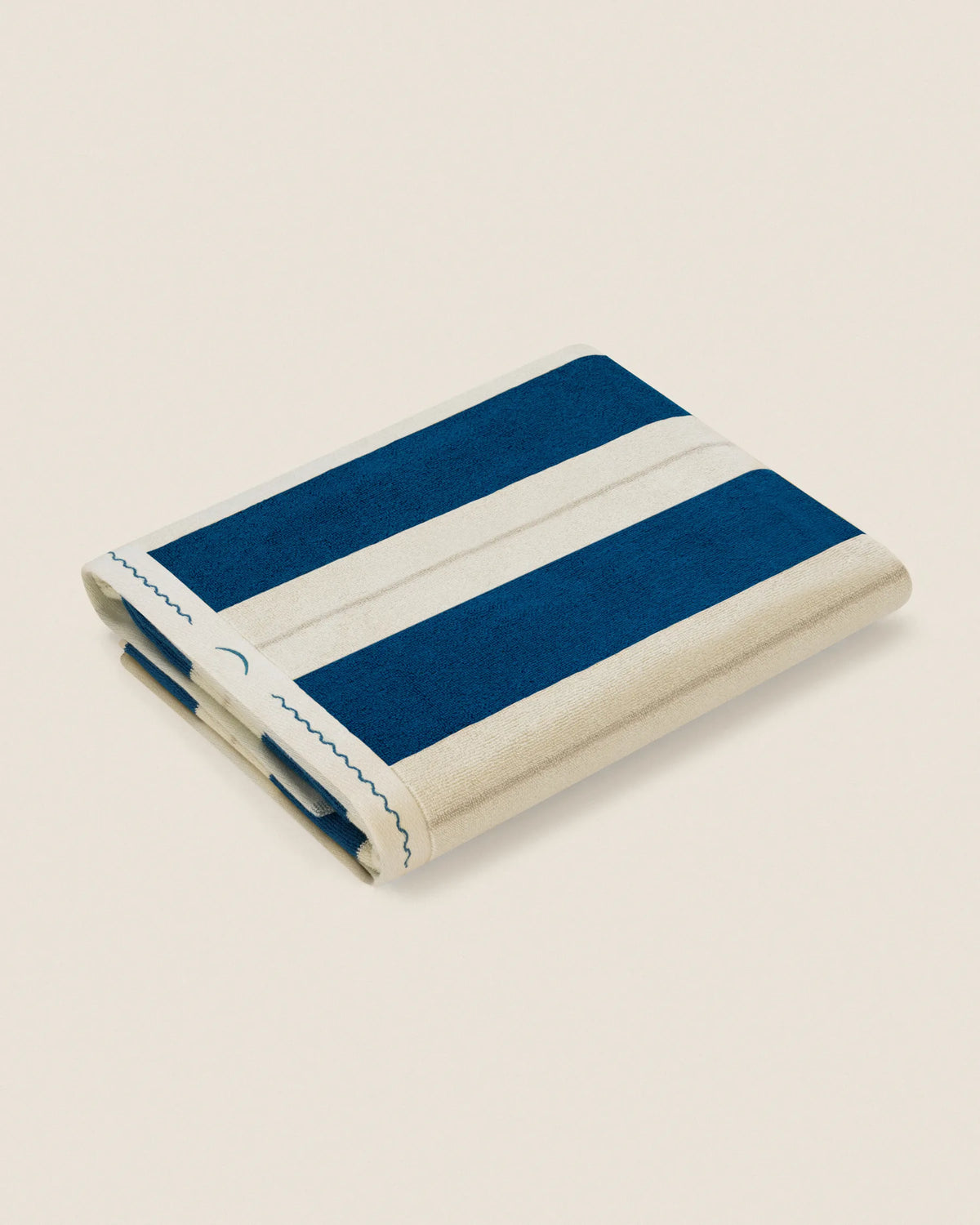 Folded Éteanne Anné striped beach towel in Ora Blu on neutral background
