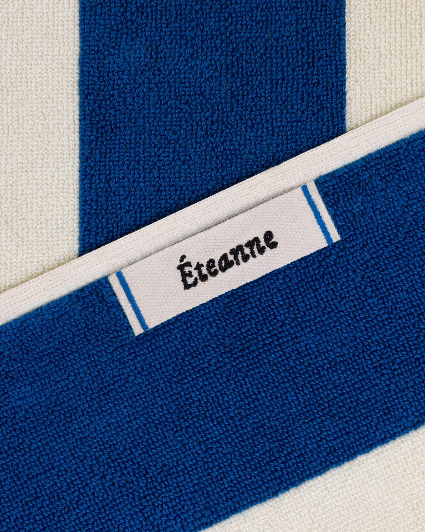 Éteanne woven label embroidered onto striped cotton beach towel in Ora Blu color