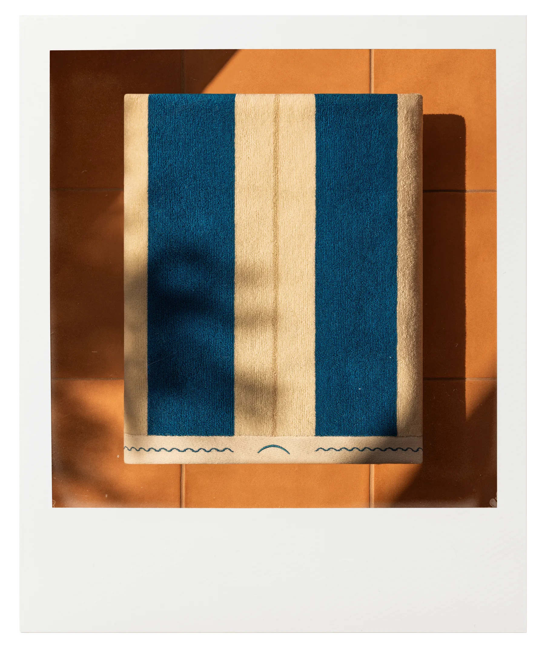 Éteanne Anné striped towel in blue and sand tones on terracotta tiles, sunlit