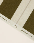 Close-up of striped beach towel edge with embroidered monogram in Terre Verte and Ionian Pearl