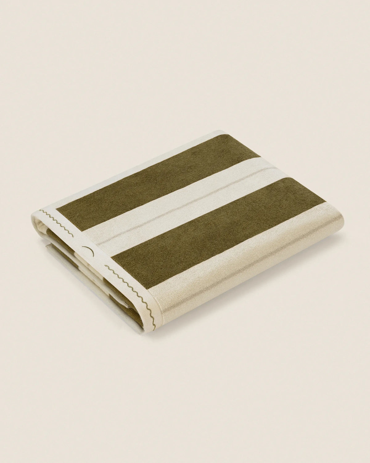 Folded Éteanne Anné striped beach towel in Terre Verte on neutral background