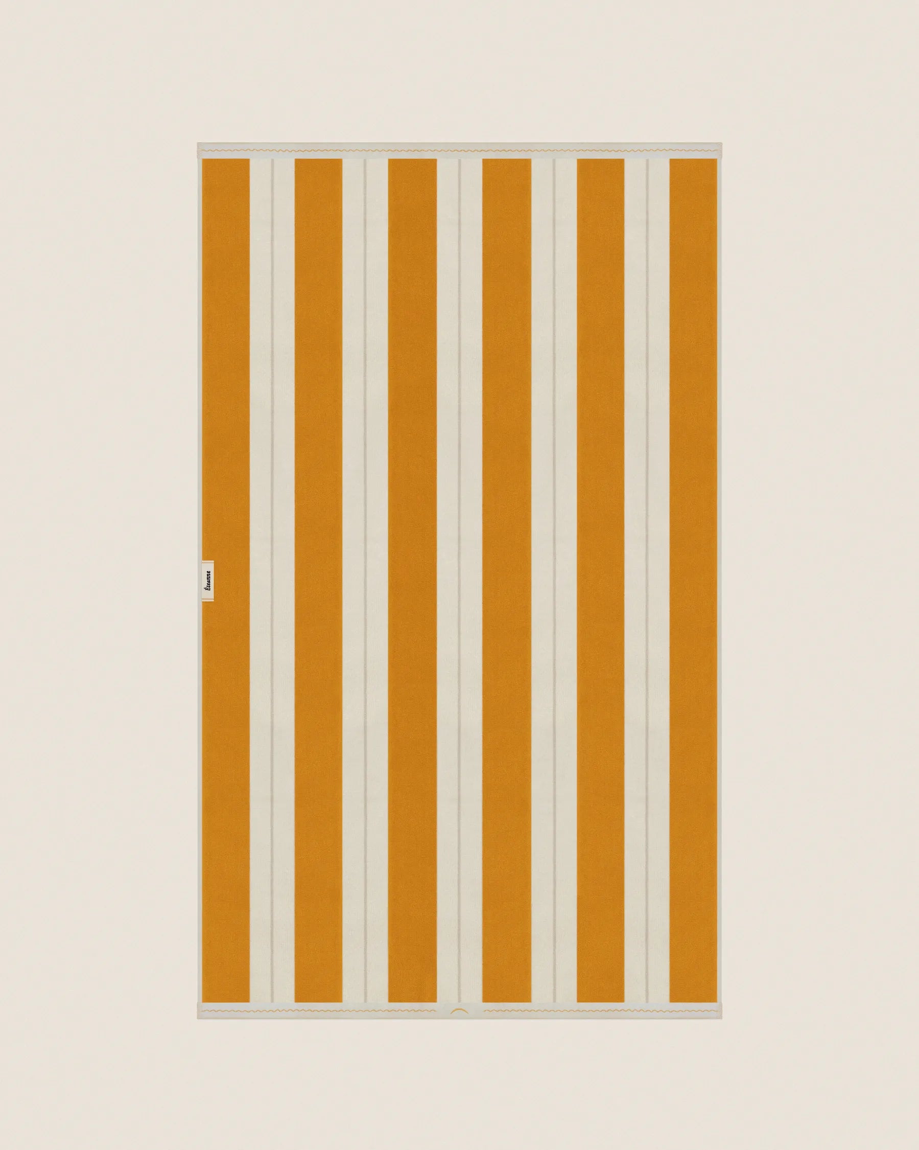 Striped beach towel in Tuscan Sun and Ioanian Pearl, laid flat on a neutral background