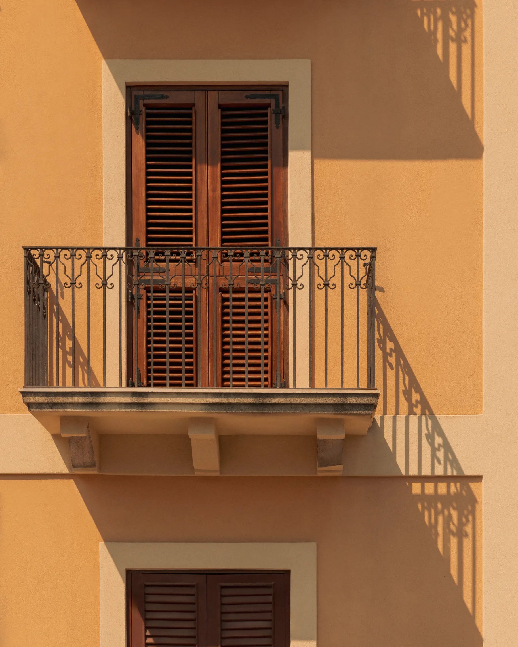 Sunlit Mediterranean balcony with wooden shutters and iron railing