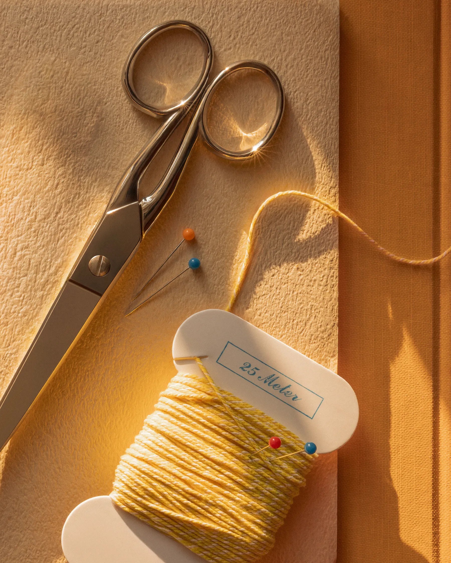 Sewing tools with yellow thread spool and pins in warm sunlight