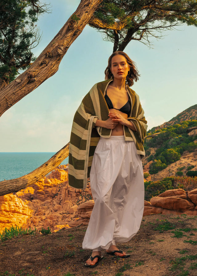 Woman wrapped in Éteanne striped beach towel in Terre Verte standing by Mediterranean coastline