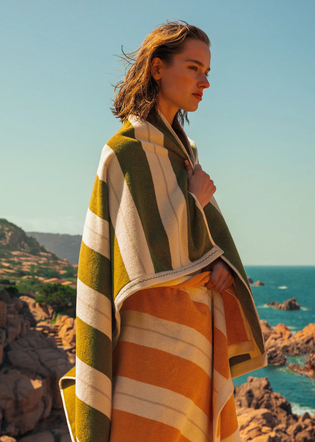 Woman wrapped in Éteanne striped beach towel in Terre Verte overlooking rocky Mediterranean coastline