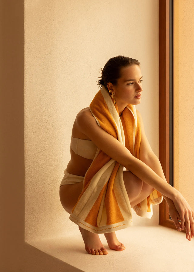 Woman wrapped in Éteanne Anné beach towel in Tuscan Sun sitting by sunlit window in Mediterranean interior