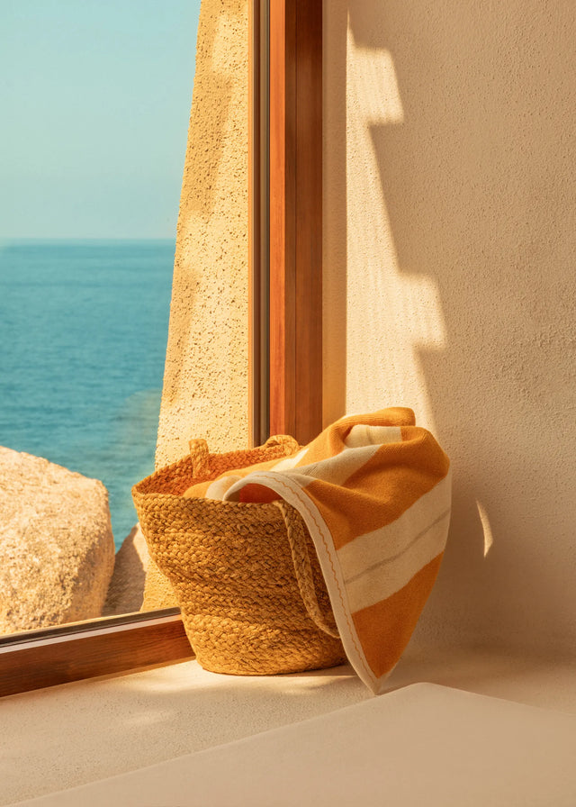 Éteanne Anné beach towel in Tuscan Sun placed in woven basket by window with sea view